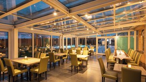 A spacious indoor dining area with a glass ceiling, multiple tables, and chairs. - FAIR RESORT All Inclusive Wellness & SPA Hotel Jena (Zollnitz)