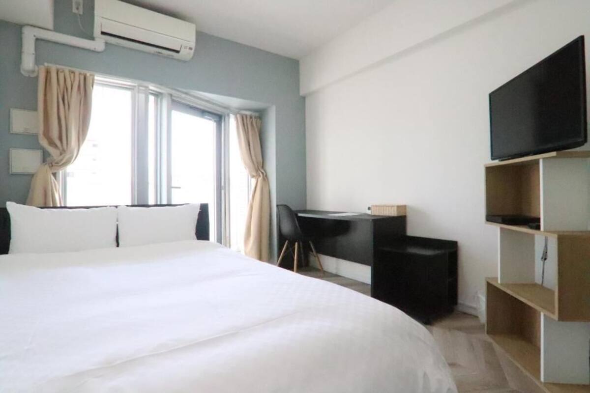A hotel room with a large bed, a desk with a chair, a television, and a window with curtains.