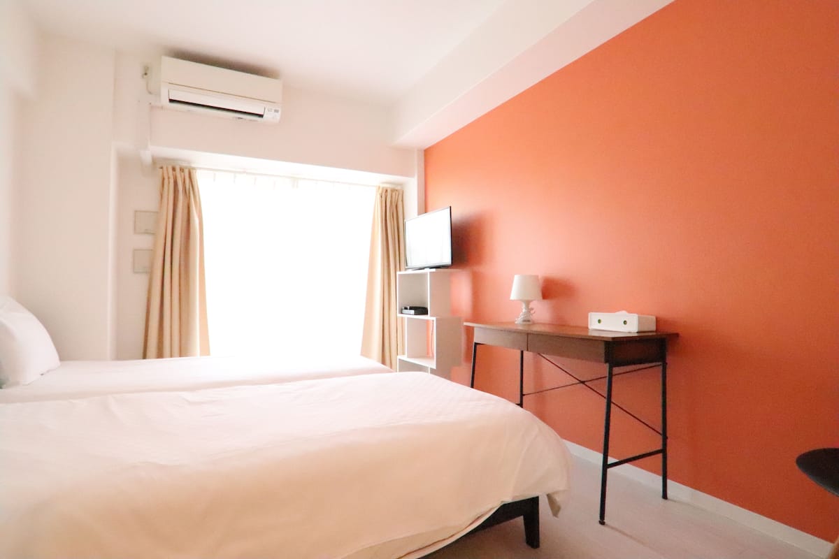 A hotel room with a bed, a desk, a television, and an air conditioning unit.