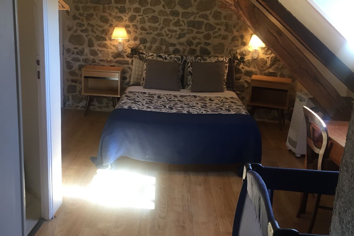 A bedroom with a stone wall, a wooden ceiling, a bed with patterned bedding, and two bedside lamps.