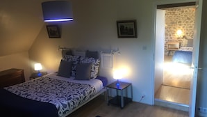 Un dormitorio con cama, mesitas de noche, lámpara y puerta que da a otra habitación.