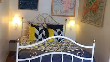 Una cama con estructura metálica blanca, un edredón estampado y dos almohadones decorativos. Hay dos lámparas de pared a cada lado de la cama.