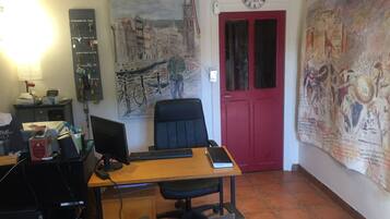 Een kamer met een bureau, computer en stoel, een rode deur, en twee grote schilderijen aan de muren.