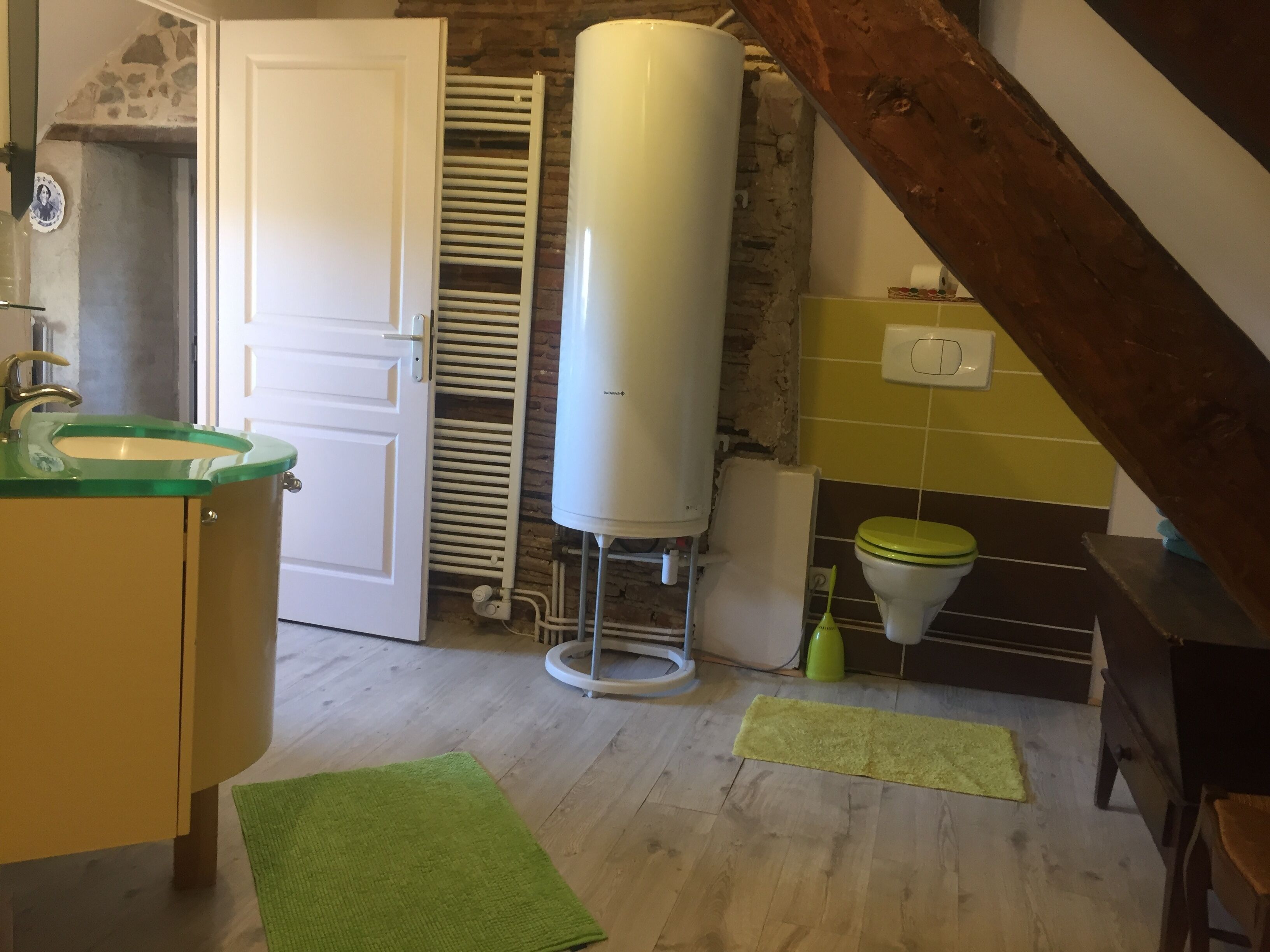 Une salle de bain avec un lavabo blanc, des toilettes, un chauffe-eau et un tapis vert sur le sol.