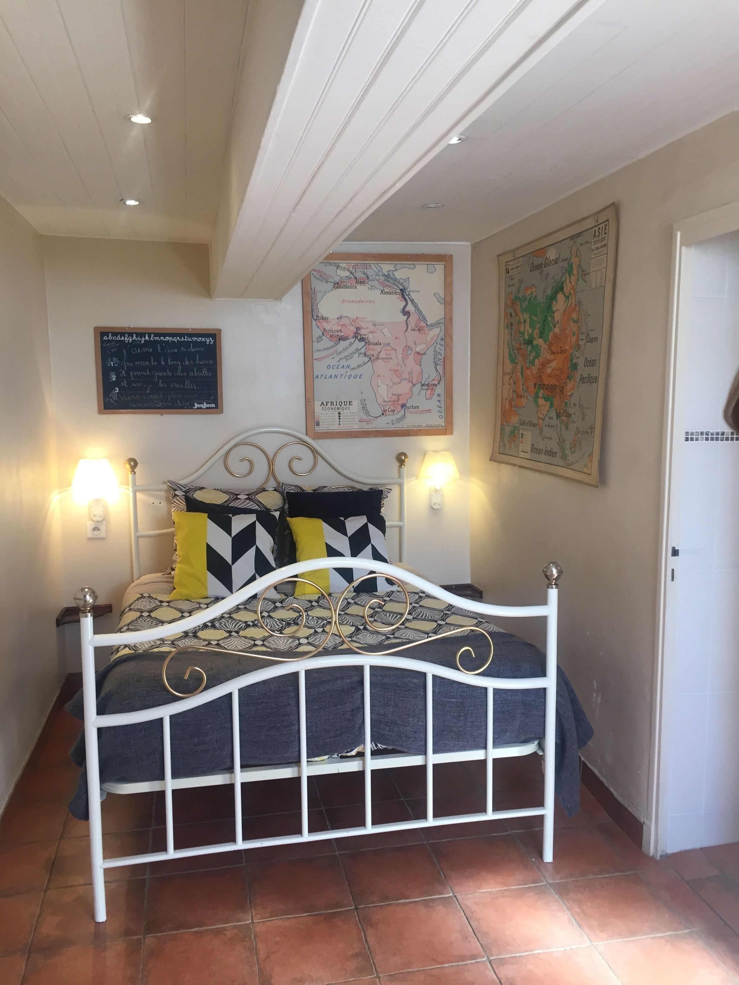 A bedroom with a bed, two wall-mounted lamps, a map, and a framed picture.