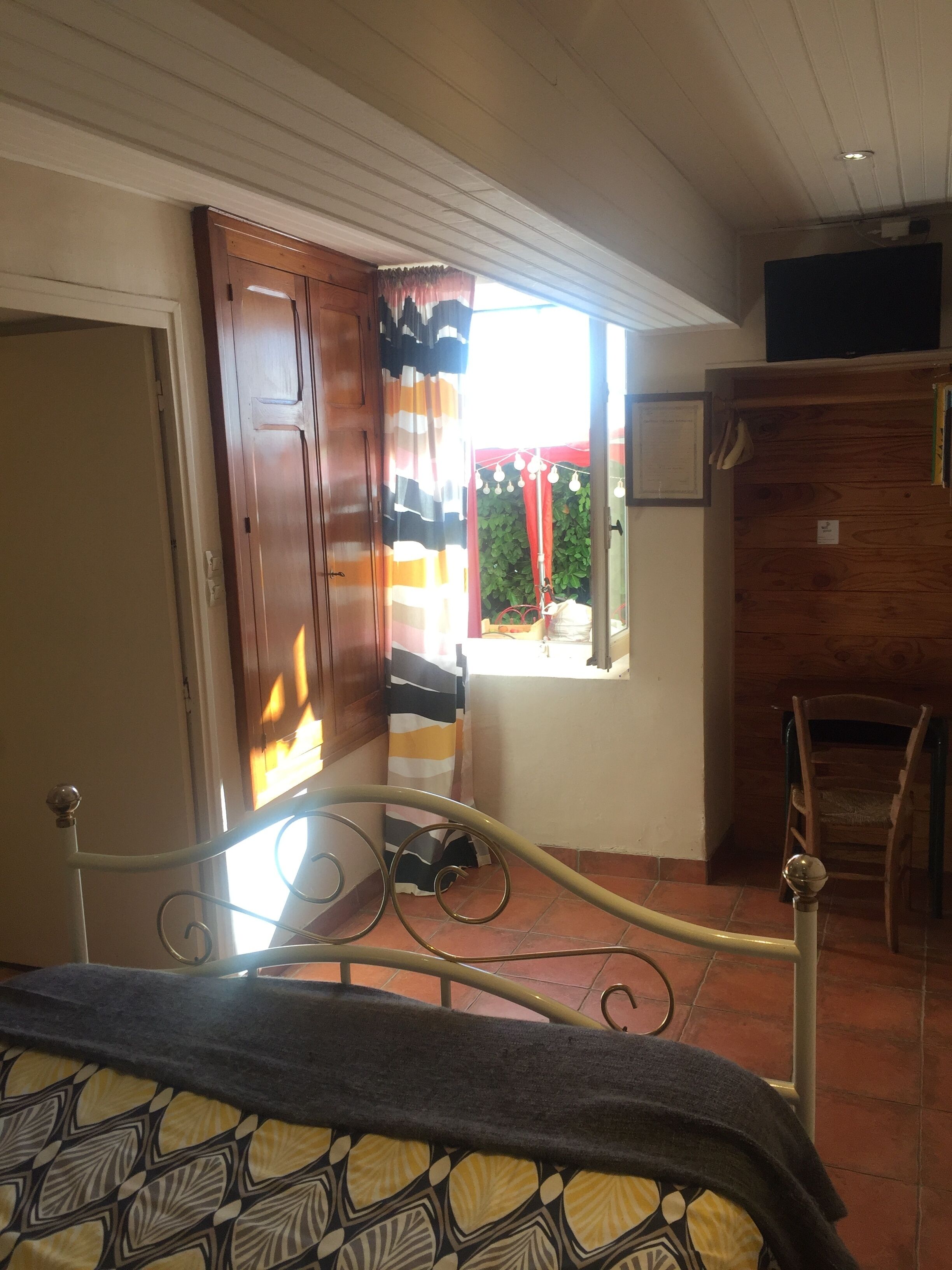 Una habitación con una cama, un armario de madera, una silla y un ventanal con cortinas.