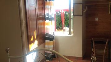Una habitación con una cama, un armario de madera, una silla y un ventanal con cortinas.
