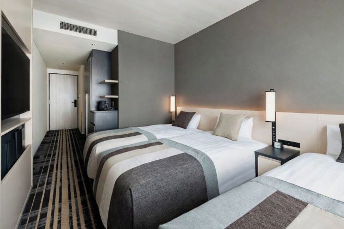 A hotel room with two beds, a TV, a desk, and a minibar.