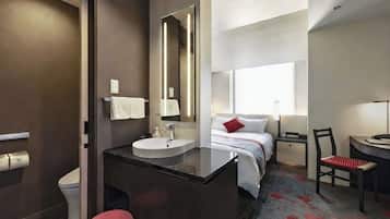 A modern hotel room with a bathroom, a bed with a red pillow, a desk with a chair, and a large mirror.