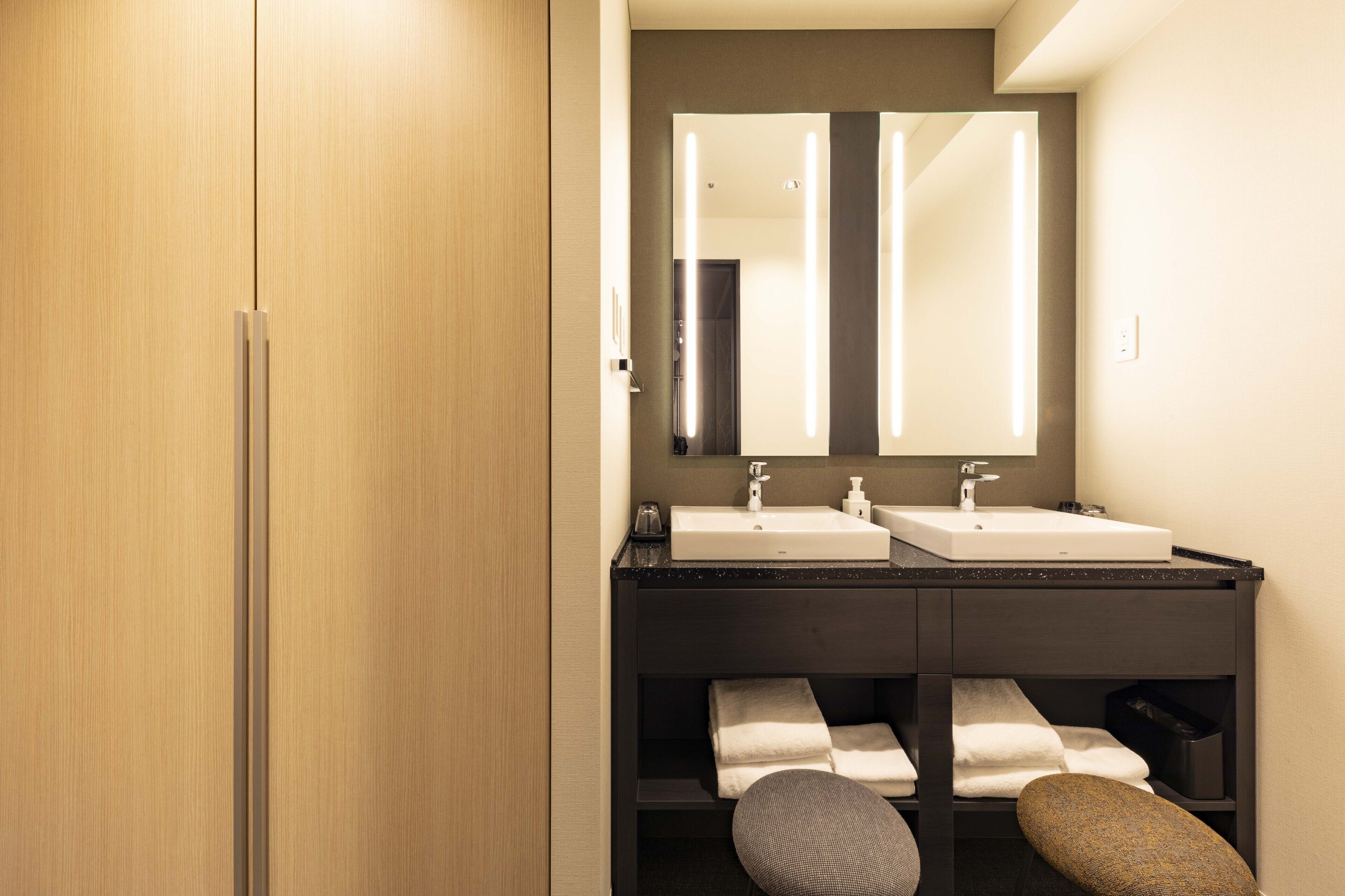 A modern bathroom with two sinks, a large mirror, and a wooden wardrobe.