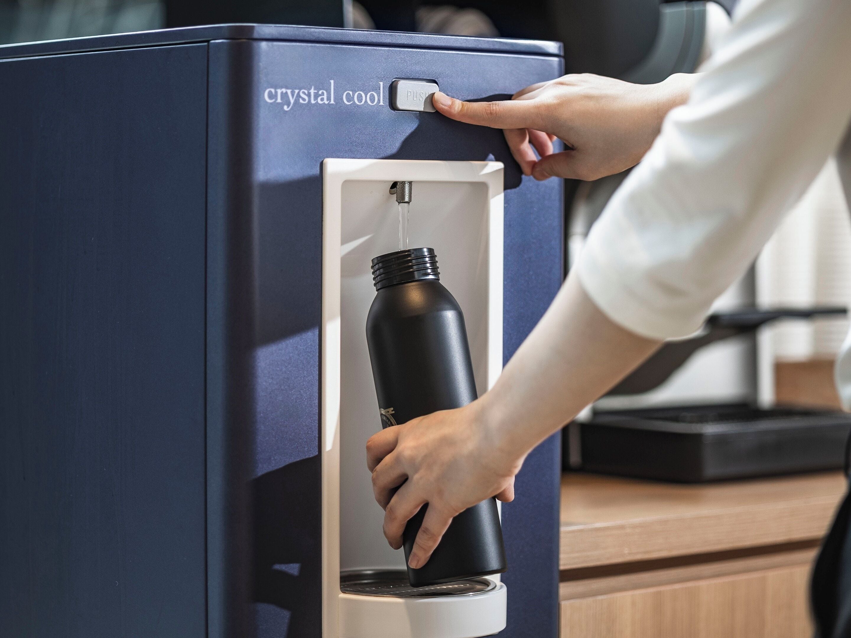 A hand inserting a black water bottle into a machine labeled 'crystal cool.'