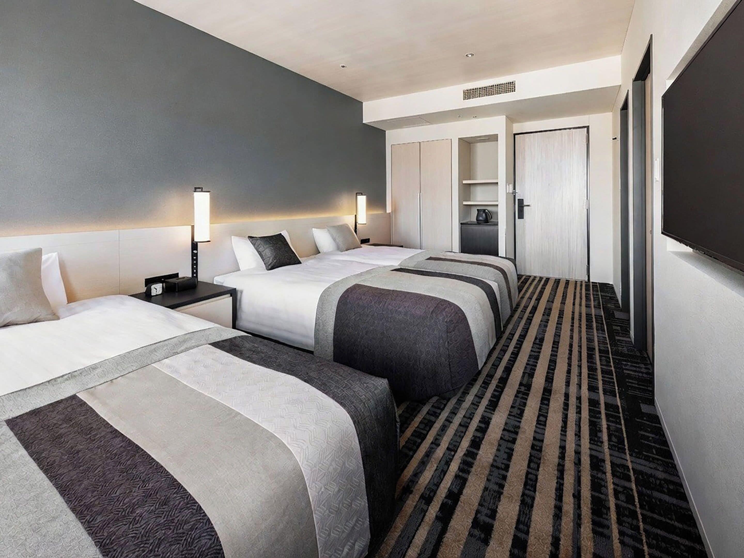 A hotel room with two beds, a flat-screen TV, a minibar, and a walk-in closet.
