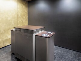 A compact, modern trash bin with a metallic finish and a textured top, placed on a dark floor against a contrasting wall.