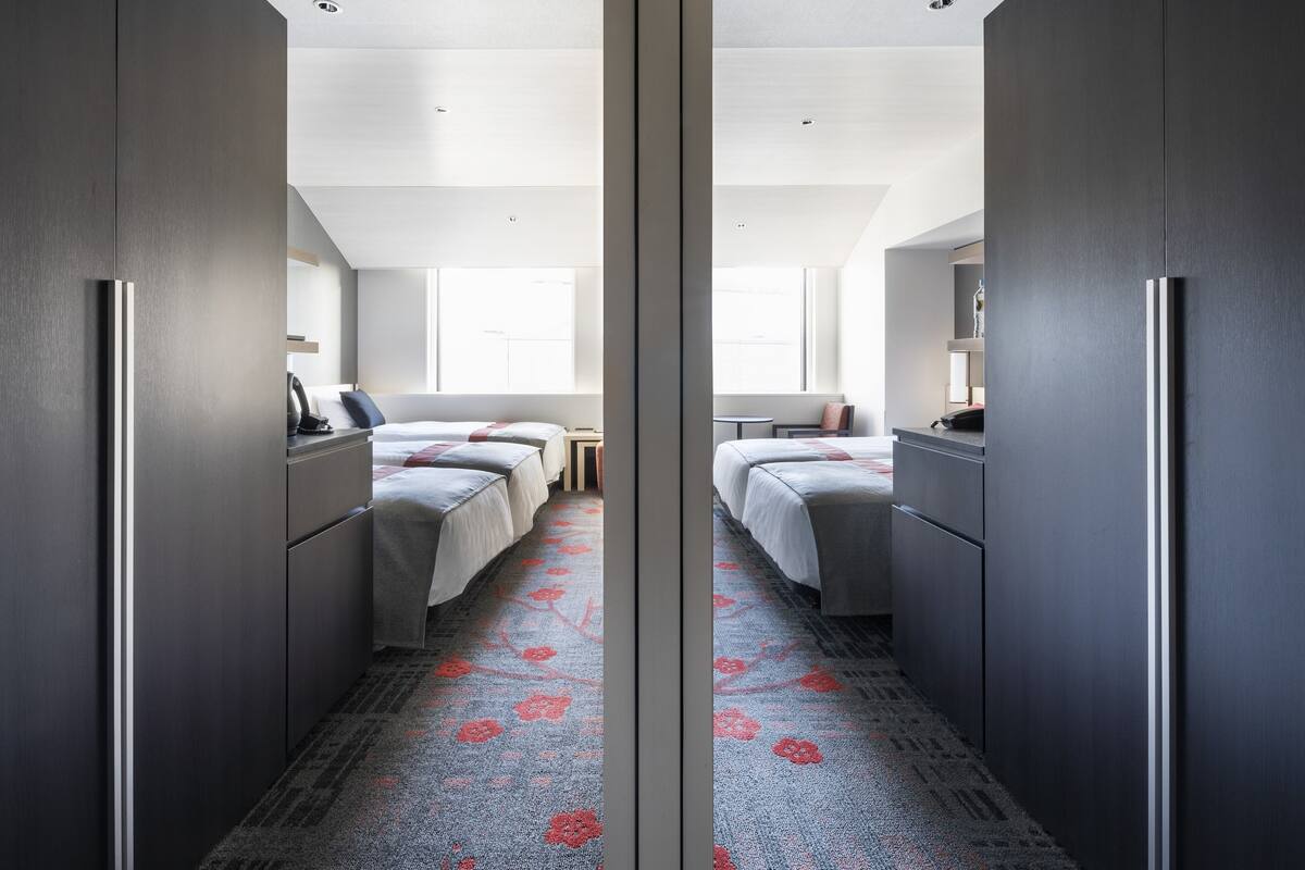 Ein Hotelzimmer mit einem Spiegelkleiderschrank, zwei Betten, einem kleinen Tisch und einem Fenster.