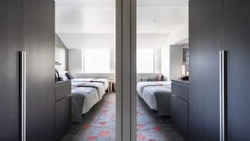 Habitación de hotel con armario espejado, dos camas, una mesita y una ventana.