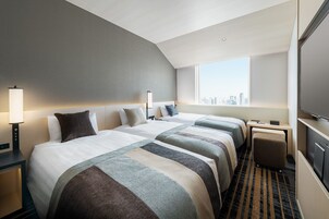 A hotel room with two beds, a desk, a chair, a TV, and a city view.