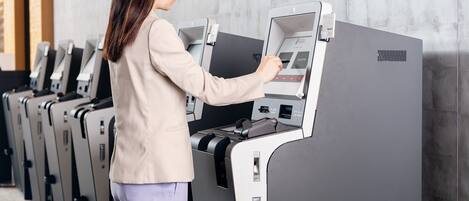 A woman using a self-service kiosk in a modern, well-lit room with a neutral color scheme and a clean, organized layout.