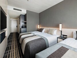 A hotel room with two beds, a TV, a desk, and a small kitchenette.
