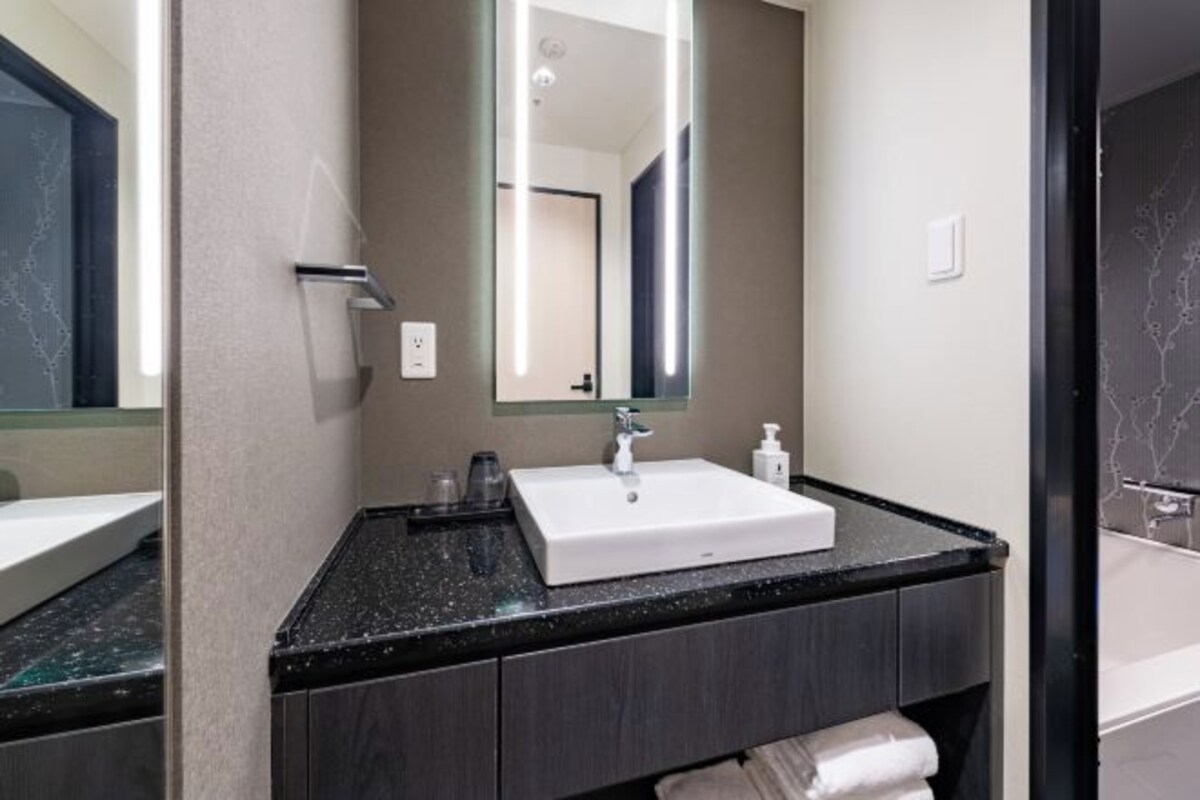 A modern bathroom with a white sink, dark countertop, and a large mirror.