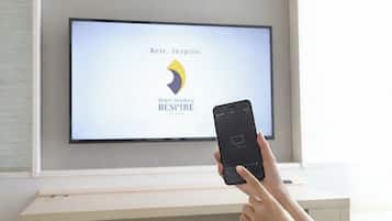 A person holding a smartphone in front of a flat-screen TV displaying the Hotel Hankyu RESPIRE logo.