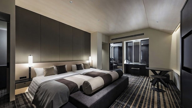 A modern hotel room with a large bed, a seating area, a desk, and a mirror.