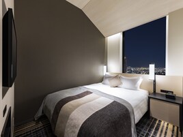 A modern hotel room with a large bed, a flat-screen TV, a nightstand, and a city view through the window.