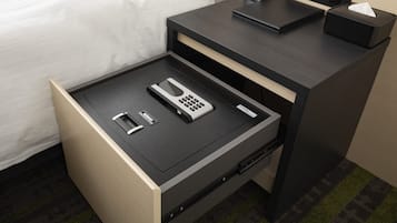 Habitación de hotel con cama, mesita de noche con un reloj, cajón con un teléfono, control remoto y caja de pañuelos.