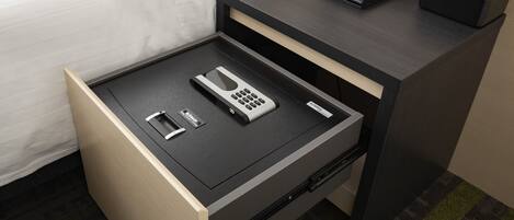 Habitación de hotel con cama, mesita de noche con un reloj, cajón con un teléfono, control remoto y caja de pañuelos.
