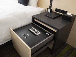 Quarto de hotel com uma cama, mesa de cabeceira com relógio, gaveta com telefone, controle remoto e caixa de lenços.