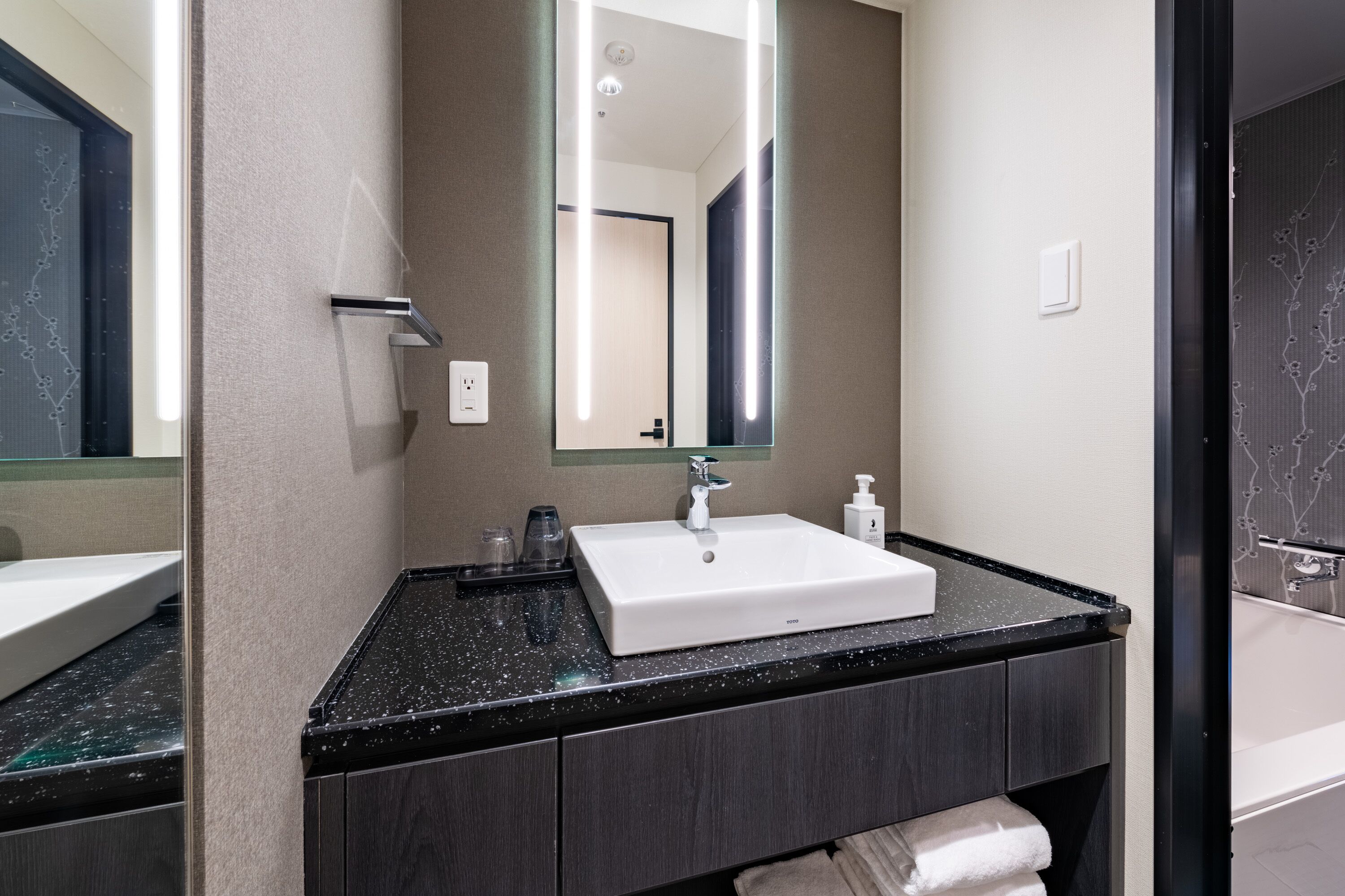 A modern bathroom with a white sink, dark countertop, and a large mirror.