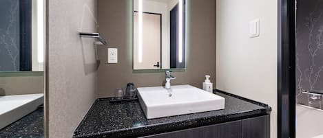 Un baño moderno con un lavamanos blanco, encimera oscura y un espejo grande.
