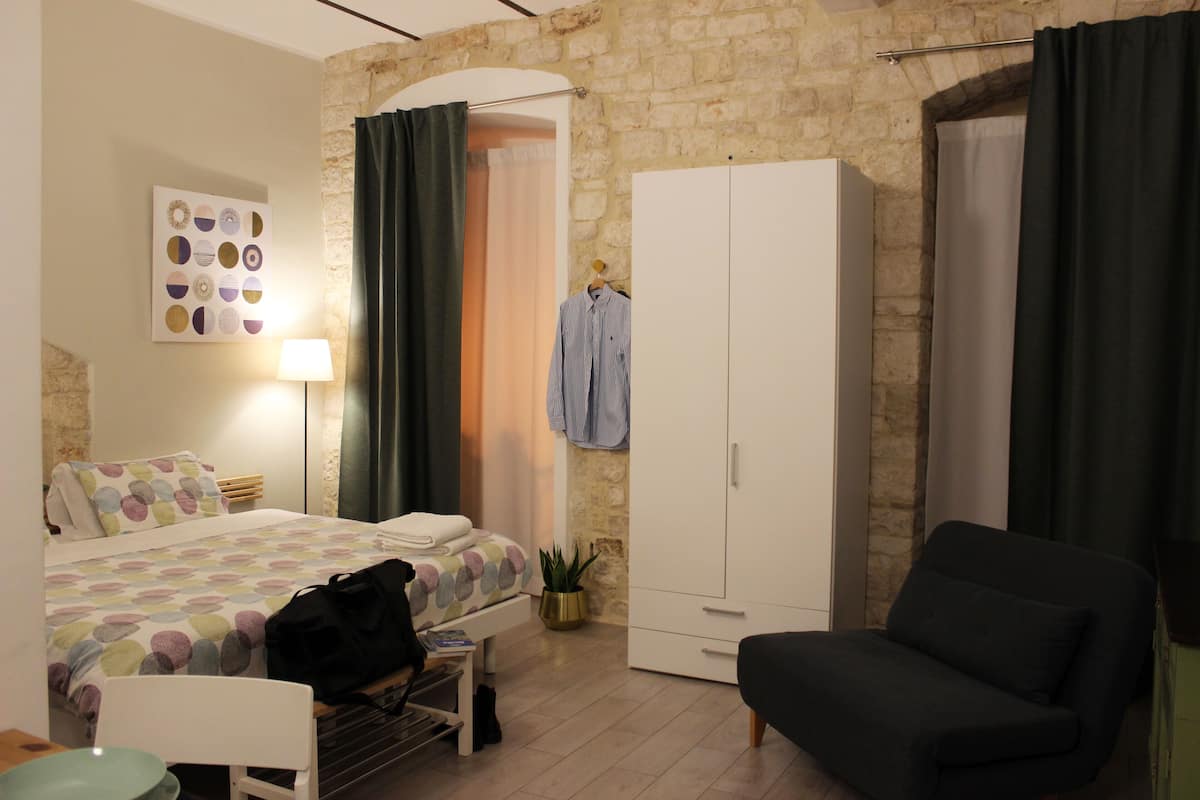 Een slaapkamer met een bed, een bureau, een stoel, een kledingkast en een potplant.