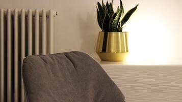 A room with a radiator, a grey chair, and a potted plant on a table.