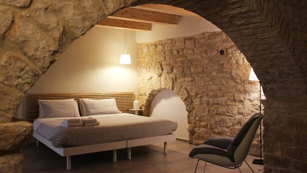 Une chambre avec un mur en pierre, un lit avec une tête de lit en bois, une table de chevet avec une lampe et une chaise.