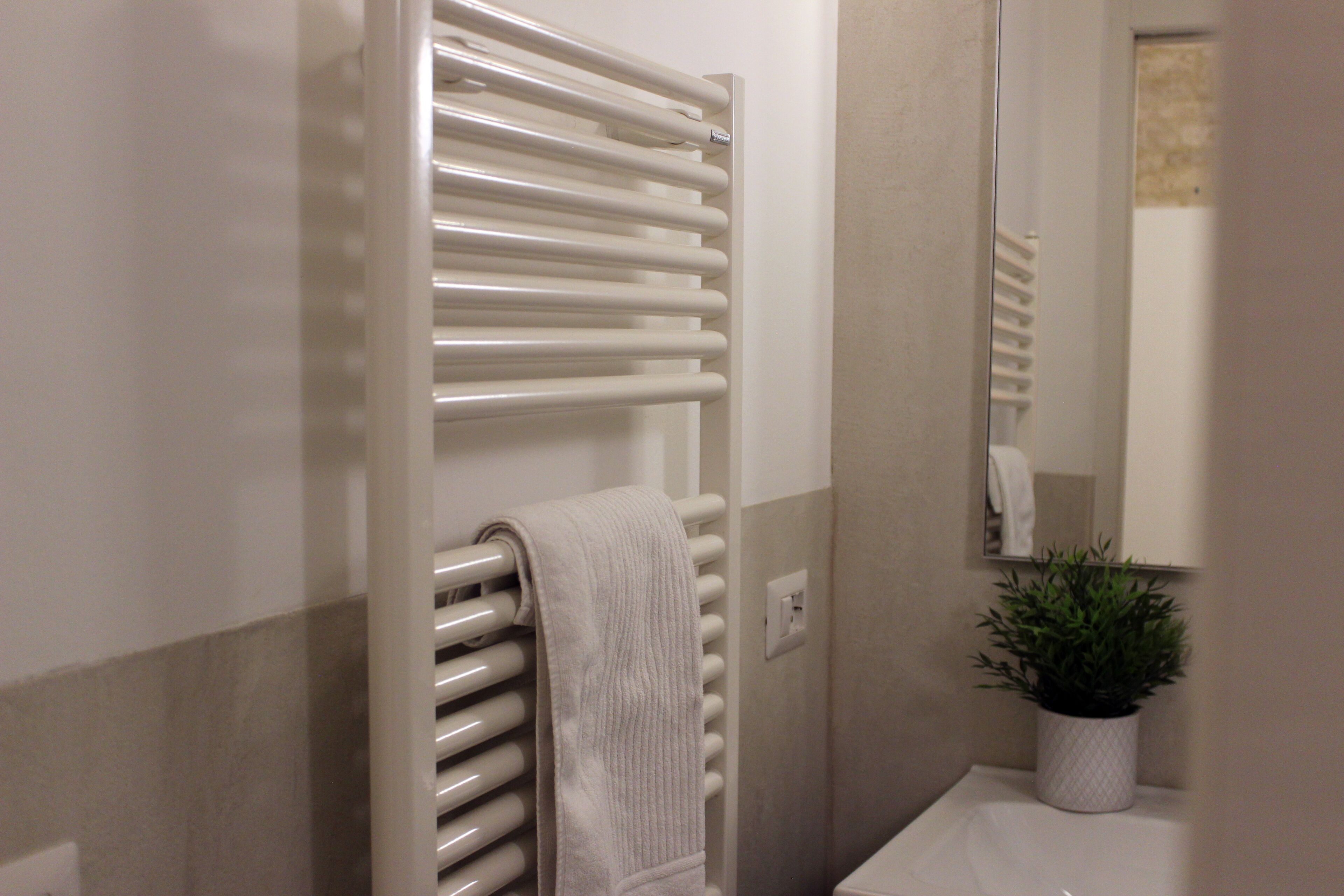 A bathroom with a white towel on a radiator, a potted plant, and a mirror reflecting a towel.