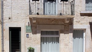 Un bâtiment en pierre doté d’un balcon, d’une porte et d’une fenêtre avec des rideaux.