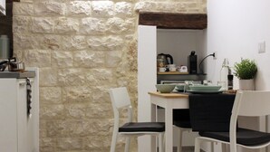 Une petite cuisine avec des chaises blanches, un mur en pierre et un plafond en bois.