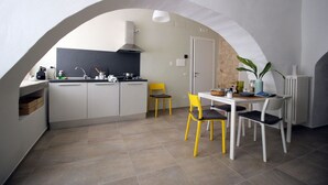 Une cuisine compacte dotée d’un îlot central, d’un coin repas avec des chaises jaunes et d’un mur d’accent en pierre.
