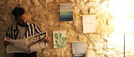 A person reading a book in front of a textured wall with various artworks displayed.