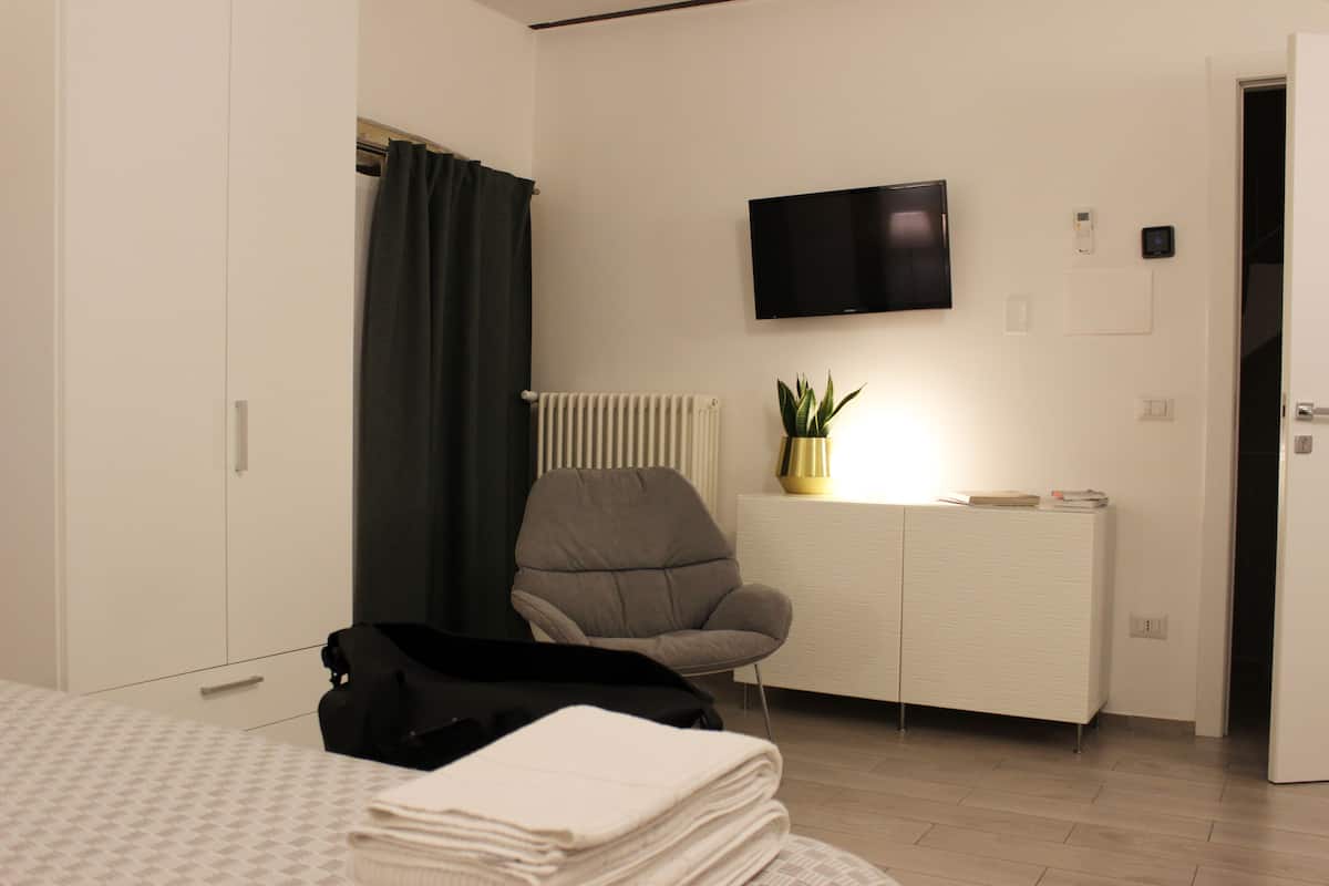 Een hotelkamer met een bed, een stoel, een televisie, een radiator en een klein kastje.