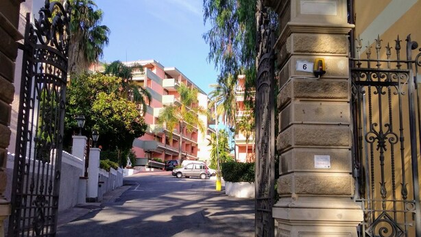 A street view with a gated entrance, a building with balconies, and a parked car. - GuestHost - Our studio is located 5 minutes walk from the beach, in the most beautiful area of Sanremo. With a small terrace with sea view and free unassigned condominium parking, (subject to availability) the apartment is waiting for you in the city of  (Sanremo)