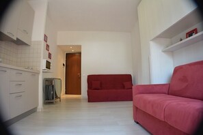 Um espaço compacto com cozinha compacta, sofá vermelho e porta que dá para outro cômodo.