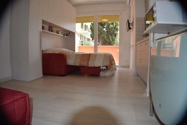 A compact room with a bed, a kitchenette, and a view of the outside.