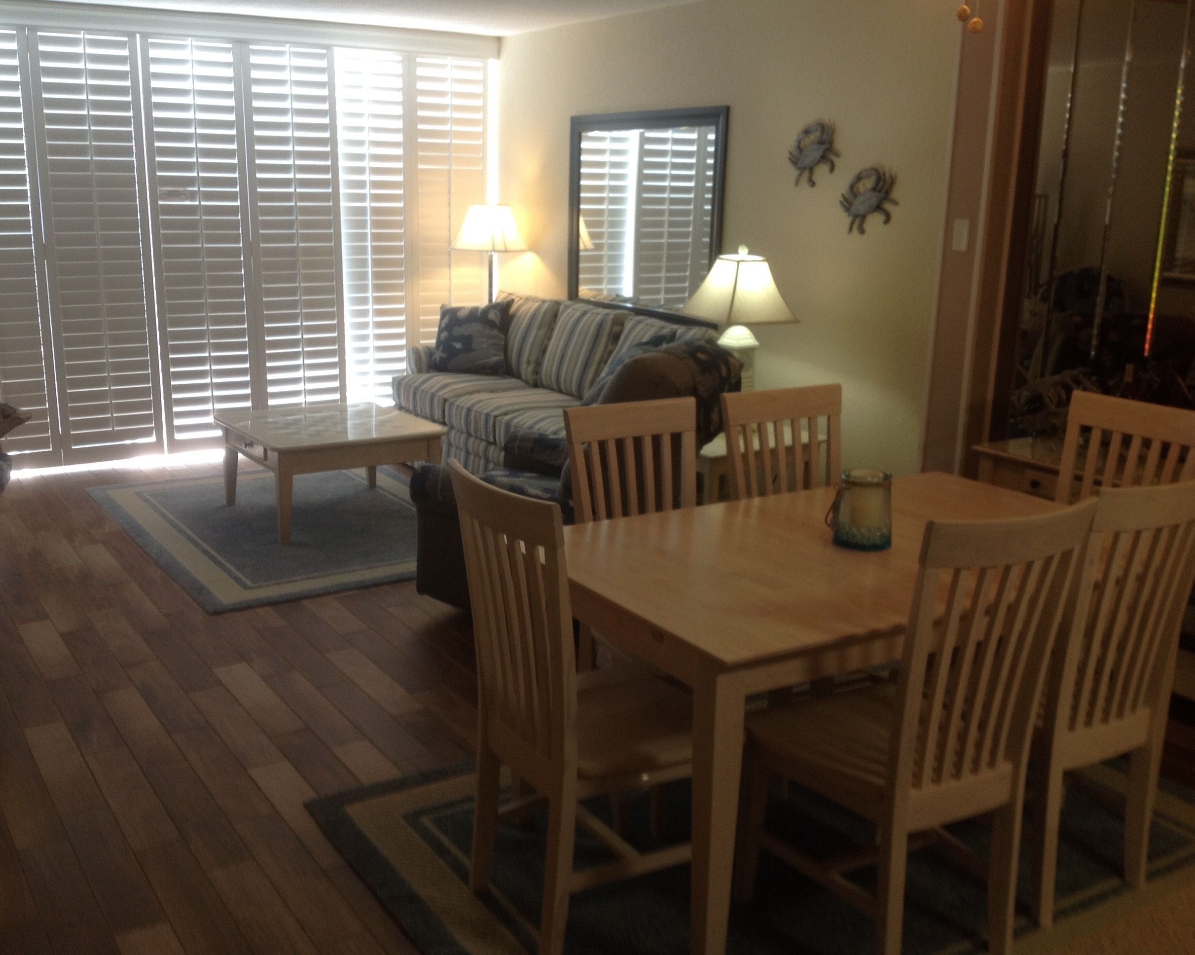Uma sala de estar com sofá, uma mesa de jantar e cadeiras. Há duas luminárias sobre a mesa.