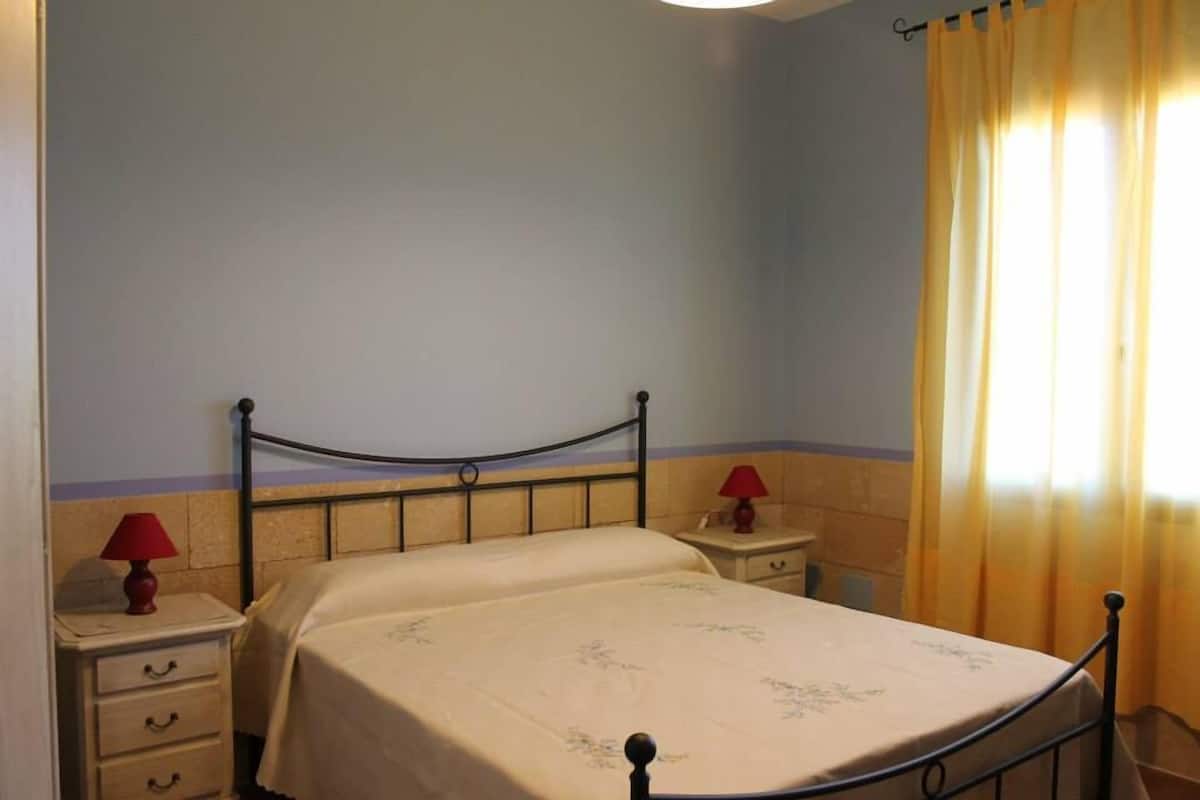 A bedroom with a bed, nightstands, and curtains.