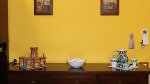 Une table en bois, sur laquelle sont posés des ustensiles de cuisine en céramique, est adossée à un mur jaune et est encadrée de deux tableaux.