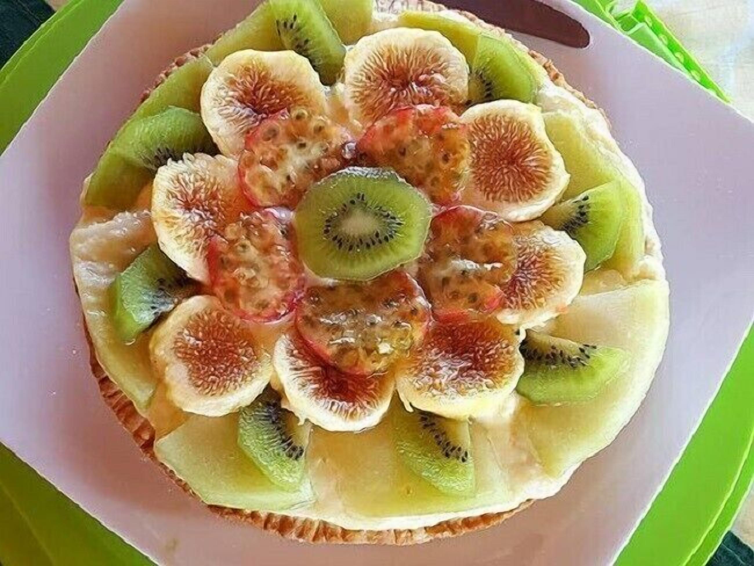 Una tarta de frutas con kiwi e higos sobre un plato rosa.