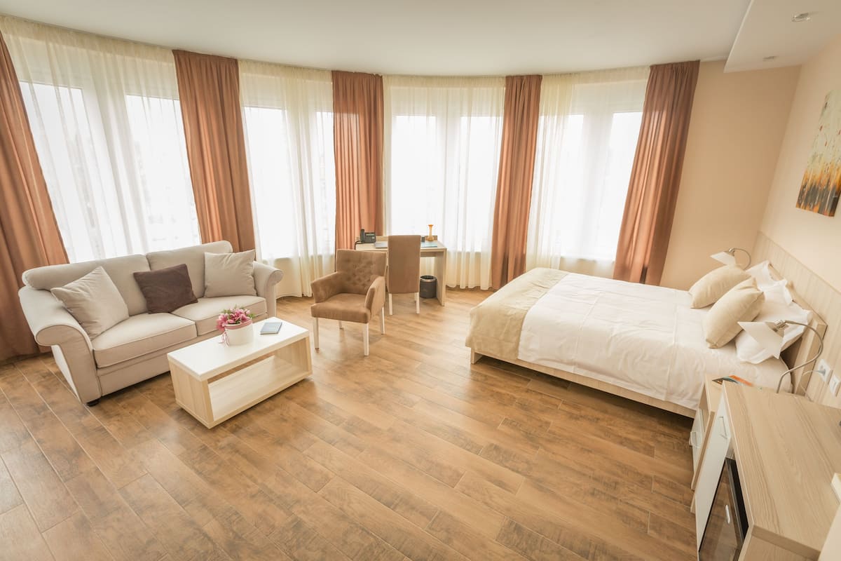 A spacious hotel room with a large bed, a sofa, a desk, and a chair.