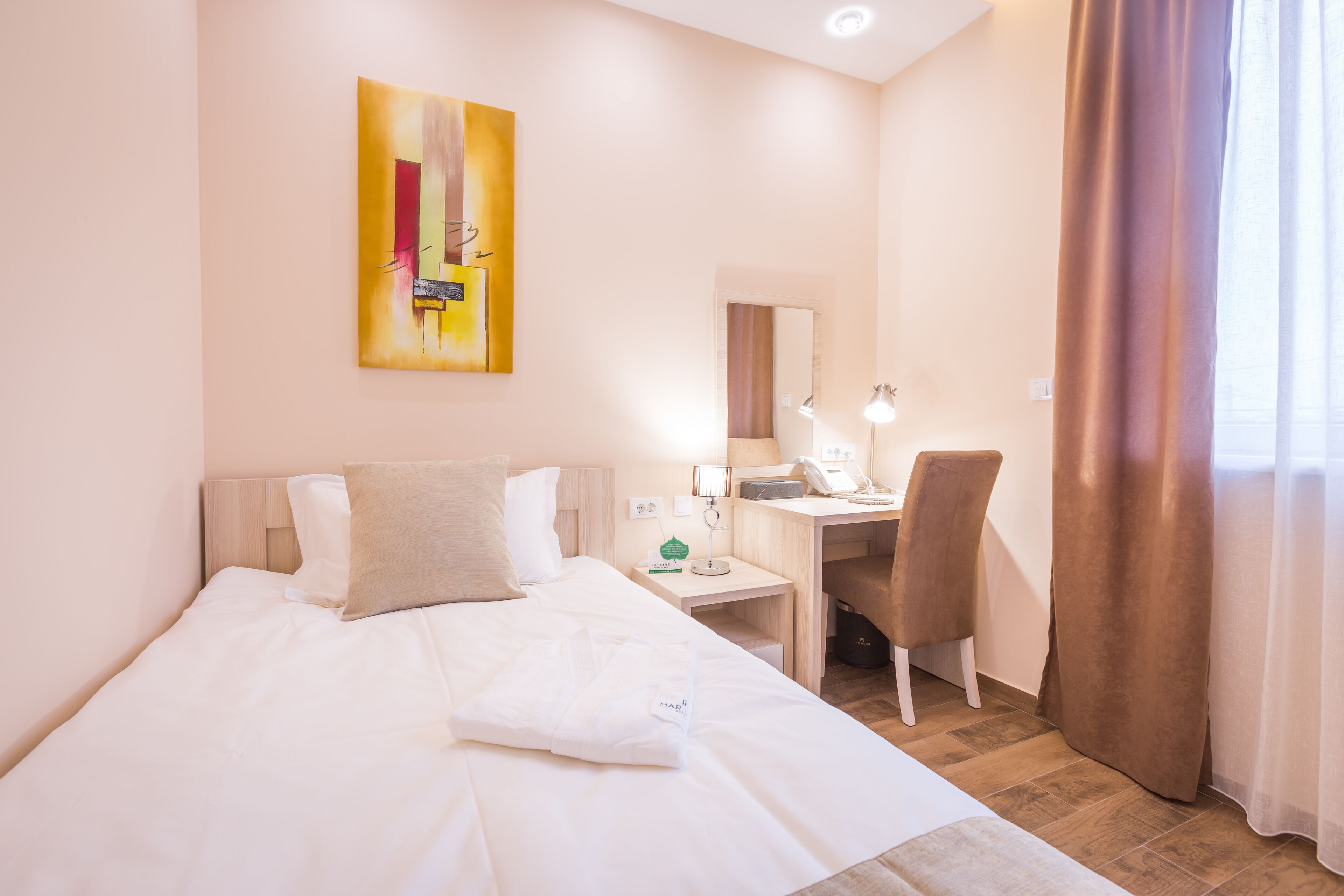 A hotel room with a bed, a desk, a chair, a lamp, and a painting on the wall.