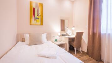 A hotel room with a bed, a desk, a chair, a lamp, and a painting on the wall.
